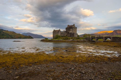 An ancient historic Eilean Donan Castle in the Western Highlands of Scotland under a cloudy sunset sky