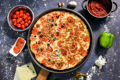 A top view of a delicious gourmet pizza on a pan with its ingredients on the table