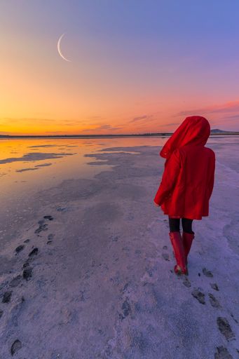 A vertical shot of a woman walking on snow with the moon shining above her