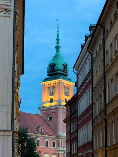 A beautifully lit church tower glows warmly against the dusky sky in Warsaw, Poland