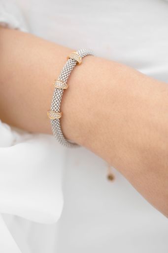 Close-up of a woman's wrist adorned with an elegant silver bracelet featuring gold accents, set against a soft white background.