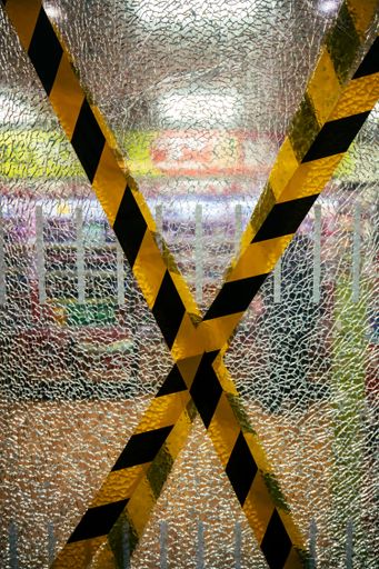 A vertical shot of a black and yellow warning tape with a crack glass in the background