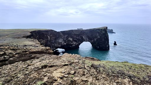 Scenic view of Dyrholaey Arch in Iceland with dramatic cliffs and ocean backdrop under a cloudy sky.