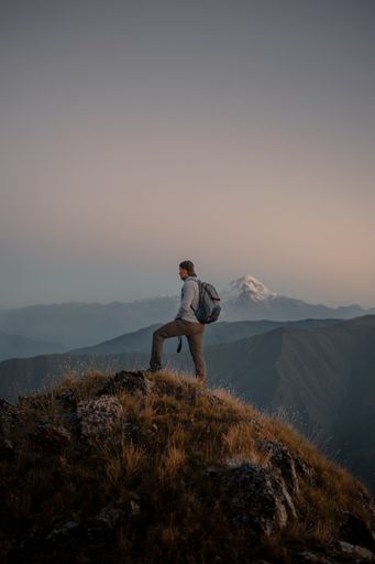 A young Caucasian male hiker standing at the top of a grassy mountain and admiring the foggy nature
