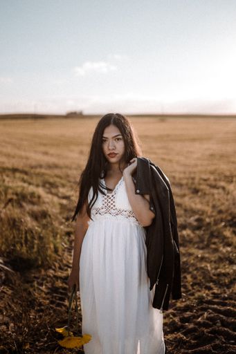 A cute brunette Hispanic woman posing in the field with flowers wearing a white elegant summer dress