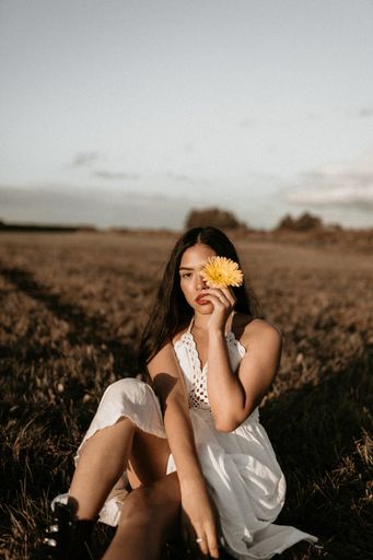 A cute brunette Hispanic woman posing in the field with a flower wearing a white elegant summer dress