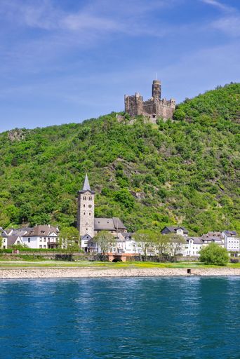 A scenic view of Katz Castle perched on a lush hilltop above the Rhine River in St. Goarshausen, Germany, under a clear blue sky.