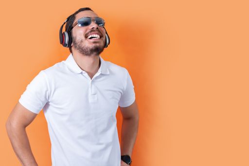A cheerful young man with beard and sunglasses, listening to music with wireless headphones
