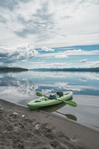 A vertical shot of a green kayak on a seashore.