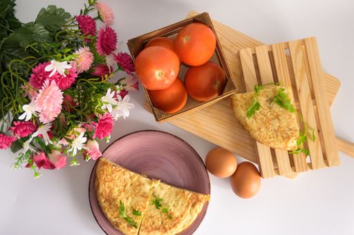 A high angle shot of half omelet, two eggs, tomatoes and a bouquet of flowers on the table