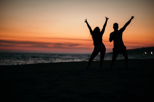 A silhouette of a crazy couple posing on a beach with a background of beautiful sunset.