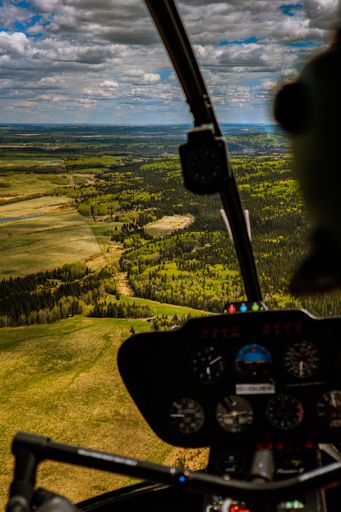 A beautiful view from a helicopter of green trees and fields under a cloudy sky