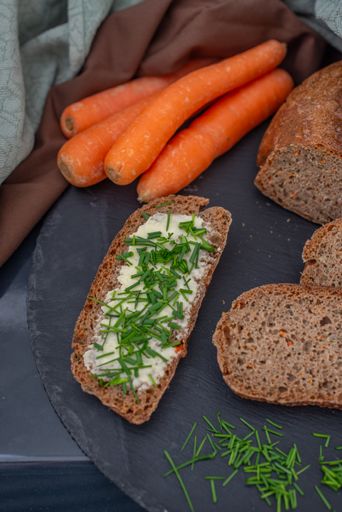A vertical shot of sliced whole wheat bread with herbs, butter, and carrots on a tray