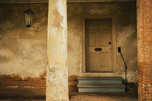 A vintage wooden door with peeling paint and a lantern on a rustic brick wall.