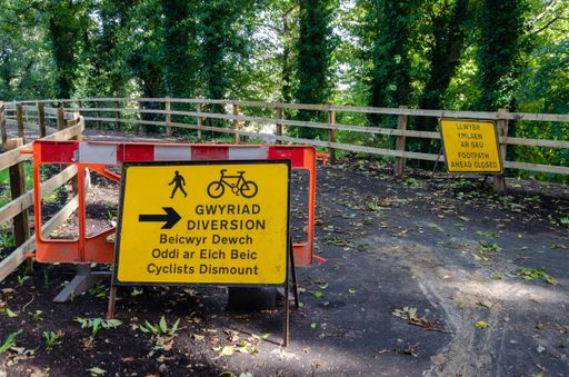 Two yellow signs placed outdoors in English and Welsh saying 'Footpath ahead closed"