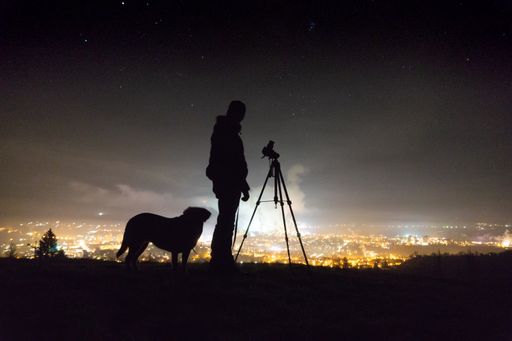 The silhouette of a man a dog and a camera at night