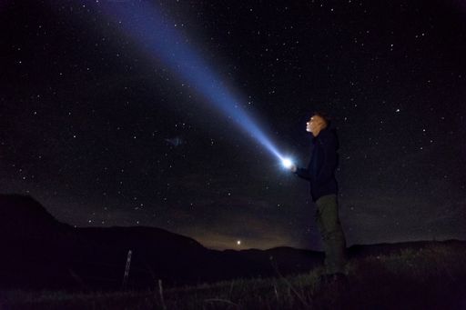 A man looking into the sky full of stars with his flash on at night