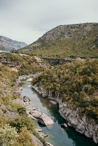 A vertical shot of a river between cliffs covered in trees in a mountainous area