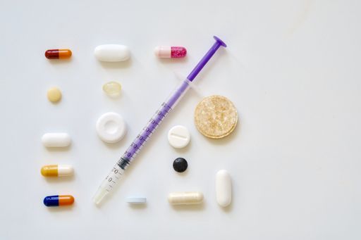 A high angle view of a syringe needle and various pills on the table under the lights