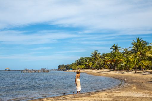 A beautiful picture of a brunette female in a swimsuit next to palms against blue lagoon at daytime in Roatan Island. Honduras
