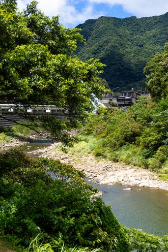A serene river landscape with lush greenery and a distant mountain under a clear blue sky.