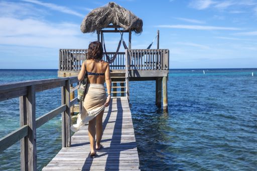 A beautiful picture of a brunette female in a swimsuit walking on the wooden bridge against wooden hut on stilts in Roatan Island. Honduras