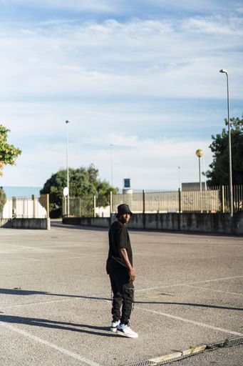 A young cool black male in a street style outfit walking in an empty parking lot