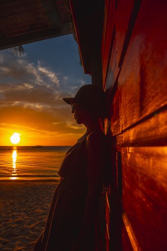 A beautiful picture of a female silhouette leaning on the wooden wall against an orange sunset in Roatan. Honduras