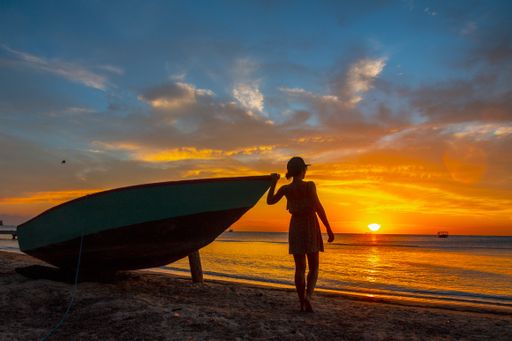 A beautiful picture of a female silhouette standing next to the boat against a mesmerizing orange sunset in Roatan. Honduras