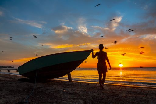 A beautiful picture of a female silhouette standing next to the boat against a mesmerizing orange sunset in Roatan. Honduras