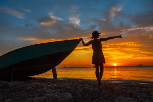 A beautiful picture of a female silhouette standing next to the boat against a mesmerizing orange sunset in Roatan. Honduras