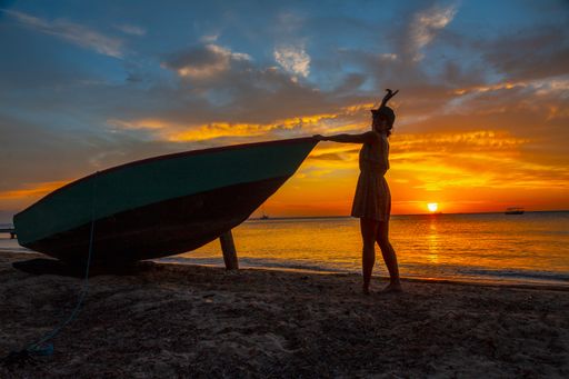 A beautiful picture of a female silhouette standing next to the boat against a mesmerizing orange sunset in Roatan. Honduras