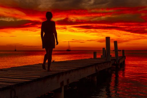 A beautiful picture of a female silhouette on a bridge against an orange sunset in Roatan. Honduras