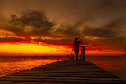 A beautiful picture of a female silhouette on a bridge against an orange sunset in Roatan. Honduras