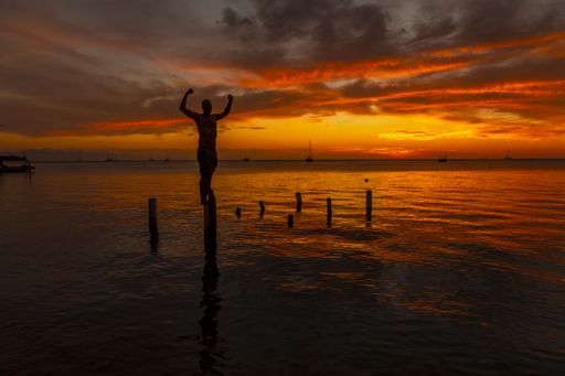 A beautiful picture of a male silhouette standing on the wooden stilts on the water against an orange sunset in Roatan. Honduras