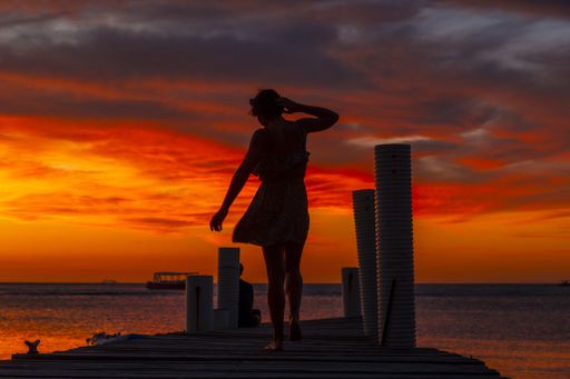 A beautiful picture of a female silhouette on a bridge against an orange sunset in Roatan. Honduras