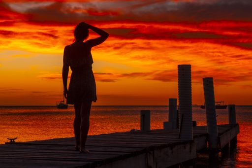 A beautiful picture of a brunette female standing on the wooden bridge against a mesmerizing sunset in Roatan Island. Honduras