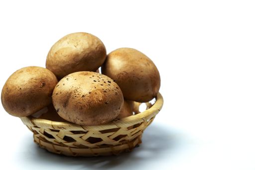 Close-up of royal brown mushrooms overflowing a small woven basket, emphasizing freshness and earthy tones against a clean white backdrop