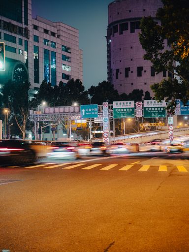 A blurry streaked image shows a busy city street at night with cars driving past.