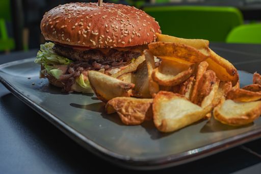 Close-up of a juicy hamburger with fresh lettuce and sliced tomatoes, served with crispy potato wedges on a modern plate.