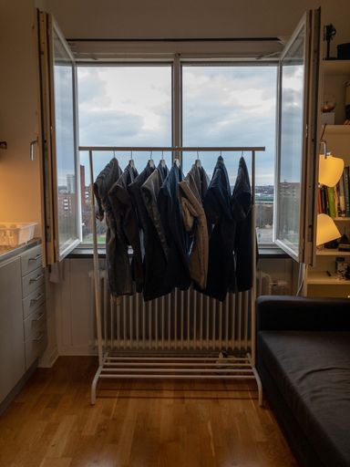 A vertical image of clothes drying on a metal rack against an open window