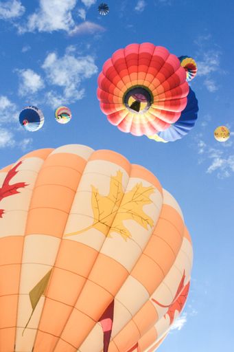A low angle shot of colorful hot air balloons rising high in the blue sky