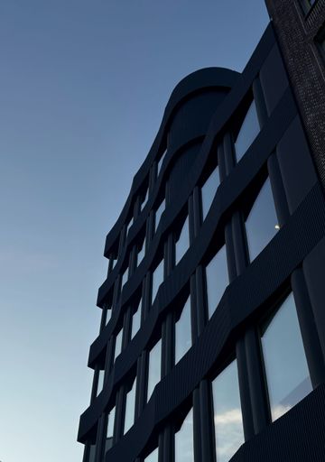Modern architectural building with wavy facade against a clear blue sky, showcasing contemporary design and urban aesthetics.