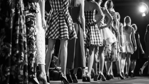Line of models walks the runway, showcasing various dress styles in a monochromatic scene.