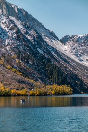 A vertical shot of a snowy mountain over the calm lake water on a sunny day