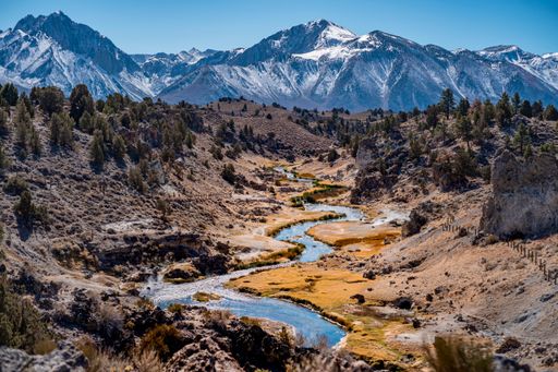 The river water flowing through rocky hills with little vegetation with snowy mountains background