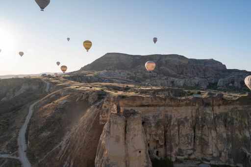 The hot air balloons soar over the rocky landscapes of Cappadocia, Turkey, under a clear blue sky during sunrise.