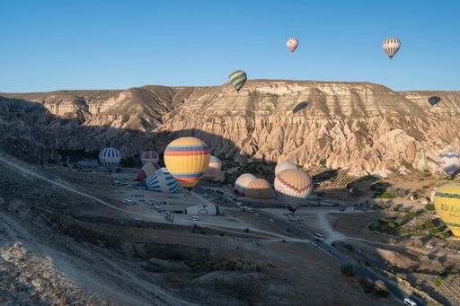 The hot air balloons soar over the stunning landscape of Cappadocia, Turkey, with rocky formations under a clear blue sky.
