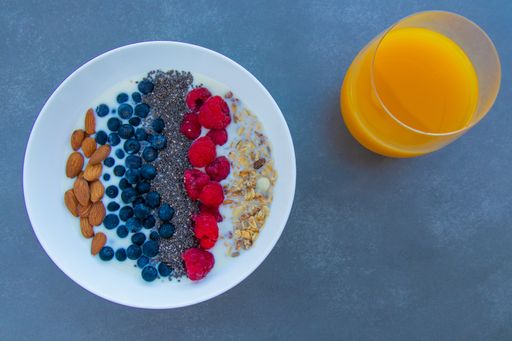 A top view of a breakfast bowl with oats, berries, chia seeds, almonds and milk and a glass of orange juice