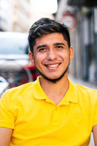 A vertical closeup of the young man sitting on a terrace looking at the camera smiling.